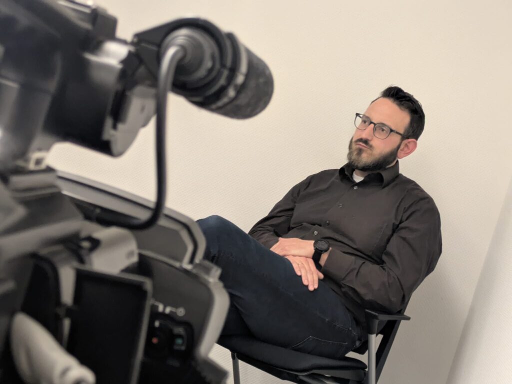 Situation beim Medientraining: Mann sitzt, Kamera ist auf ihn gerichtet.